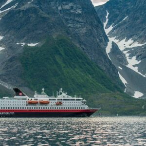 Hurtigrutens fartyg MS Nordnorge, med majestätiska berg i bakgrunden.
