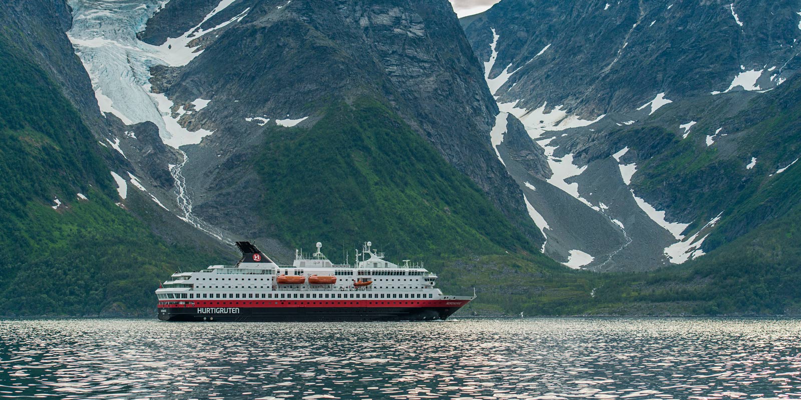 Hurtigrutens fartyg MS Nordnorge, med majestätiska berg i bakgrunden.