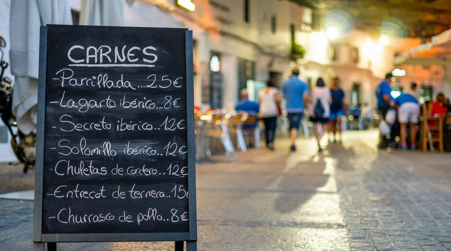 Mysig gata i Spanien, kvällstid med människor på väg till middag. En skylt som bjuder in till en restaurang.