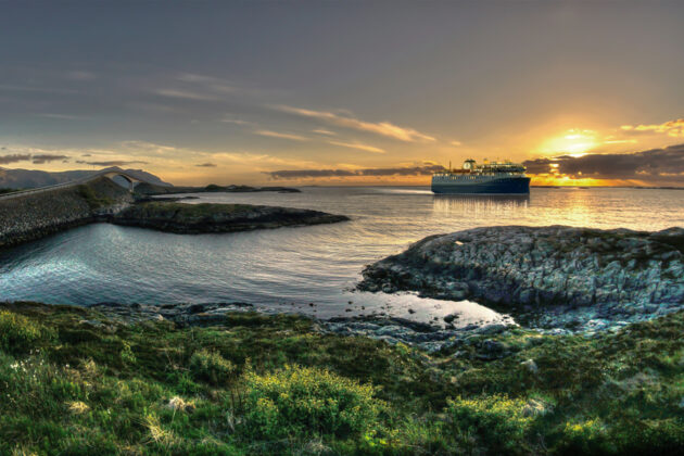 Solnedgång vid Atlantic Ocean Road i Norge, med Havila Voyages ena fartyg i närheten.